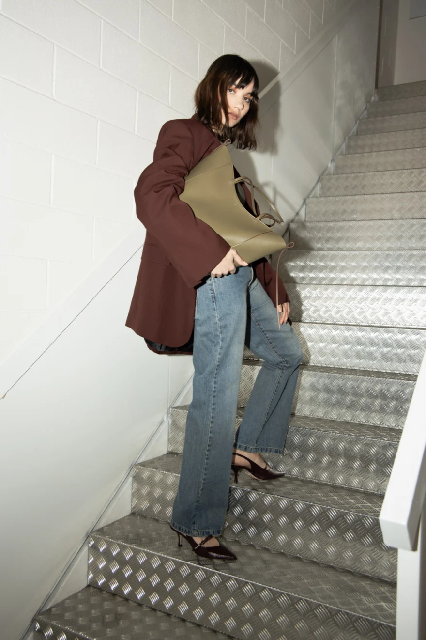 Model descending metal stairs with an olive bag, Noesi campaign photographed by Ina Cenusa