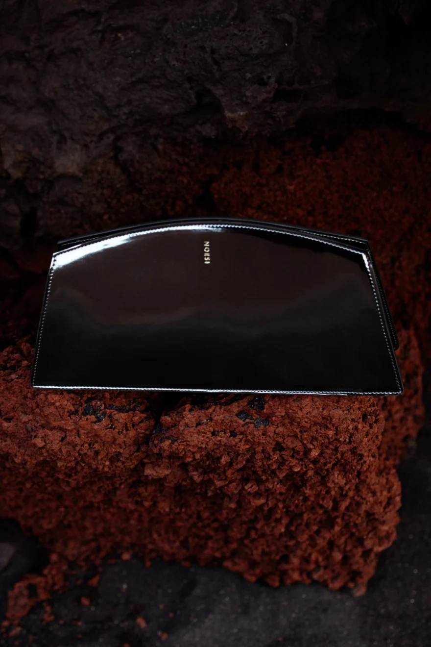 Mirror finish clutch set into dark lava stone beside rust red rock, Noesi campaign photographed by Ina Cenusa