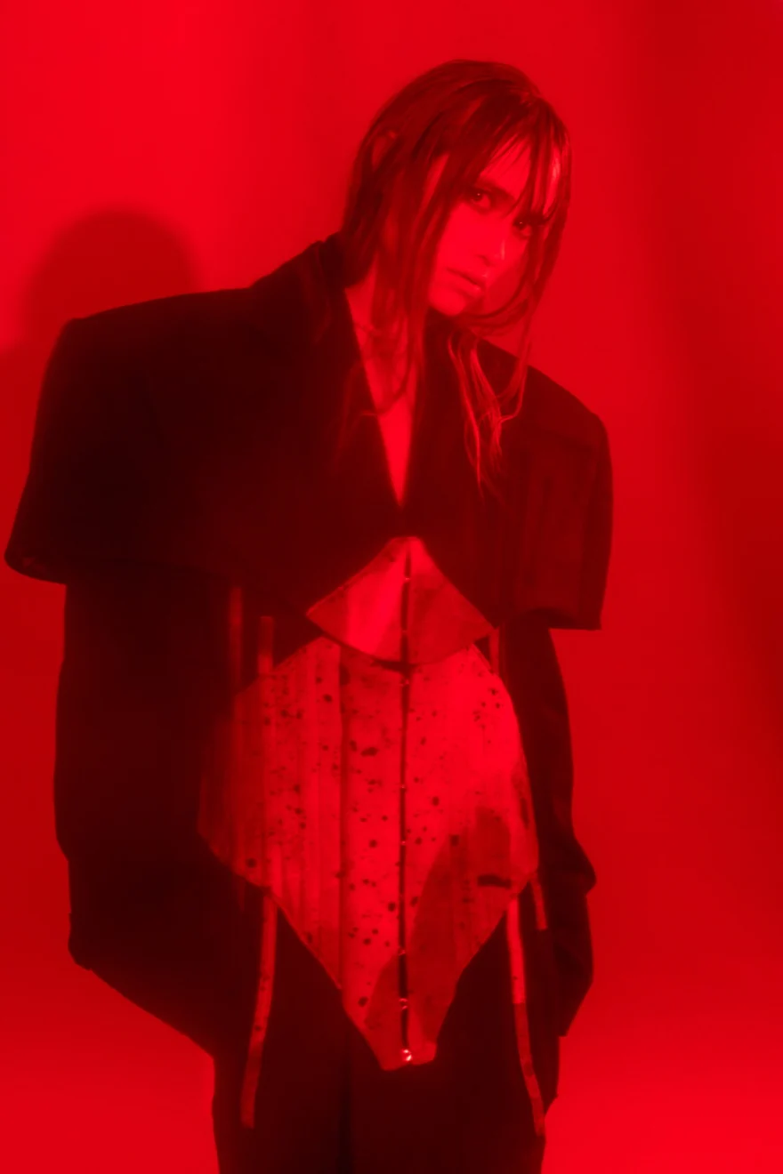 Portrait in deep red light wearing a dark jacket over a corset, SHOT Magazine editorial photographed by Ina Cenusa