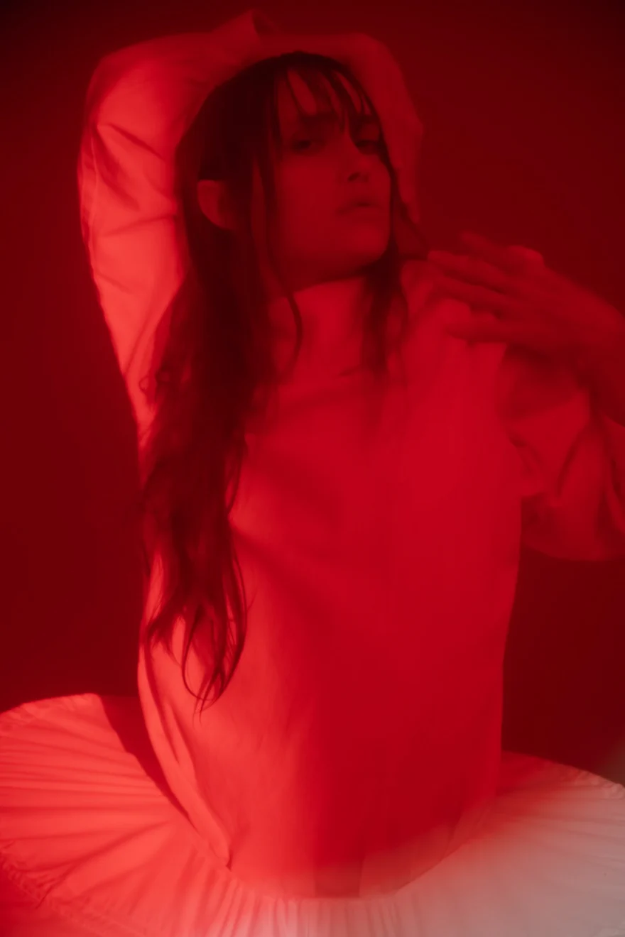 Dancer in a pleated white look bathed in red light, SHOT Magazine editorial photographed by Ina Cenusa