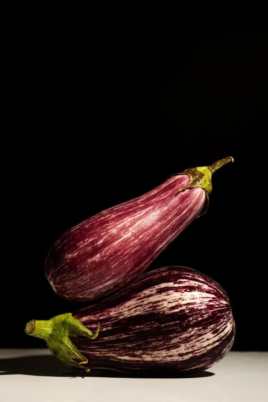 Two aubergines standing against a soft grey backdrop, Fuoco Sacro campaign photographed by Ina Cenusa