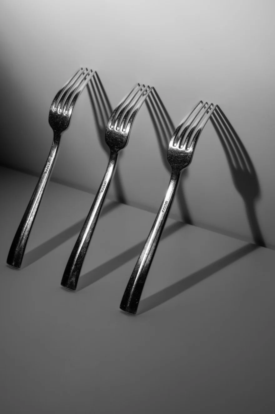 Four forks standing upright with long shadows on grey, Fuoco Sacro campaign photographed by Ina Cenusa