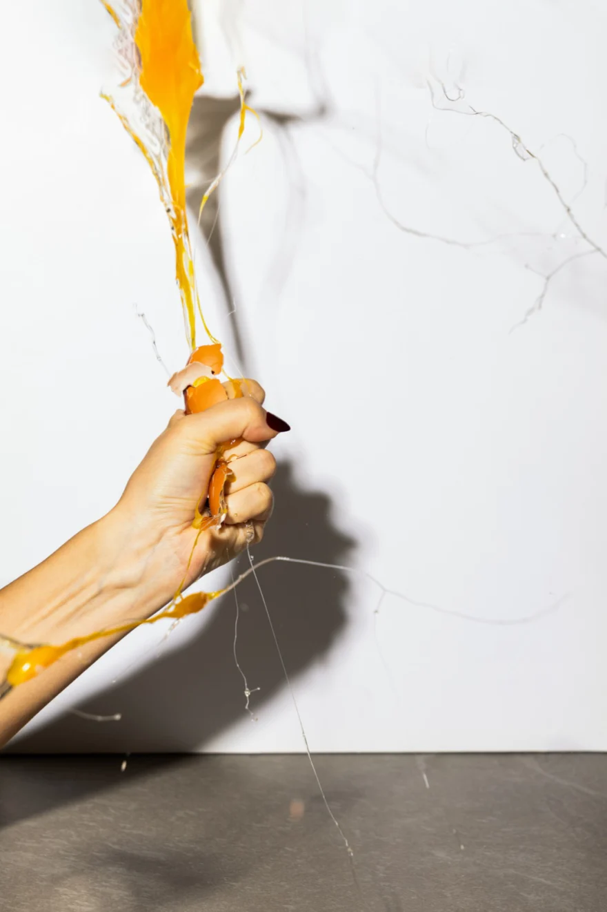 Hand crushing an orange fruit against a marble wall, juice splashing, Fuoco Sacro campaign photographed by Ina Cenusa