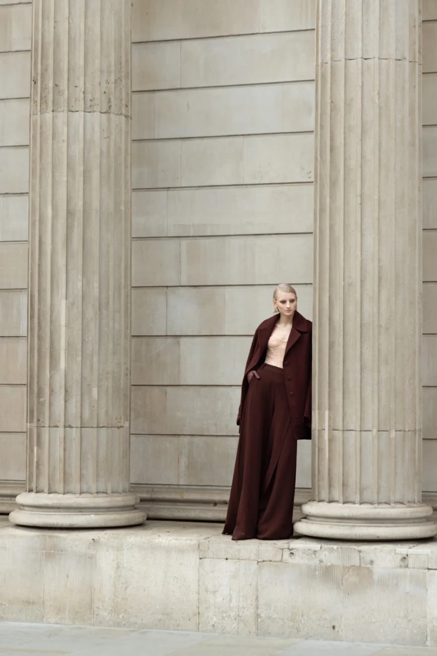 Model in a burgundy coat beside a tall stone column, Ermanno Scervino campaign photographed by Ina Cenusa