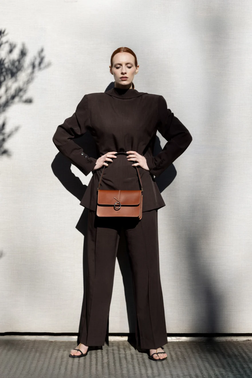 Model in a brown knit and wide trousers holding a tan clutch, Biebi campaign photographed by Ina Cenusa