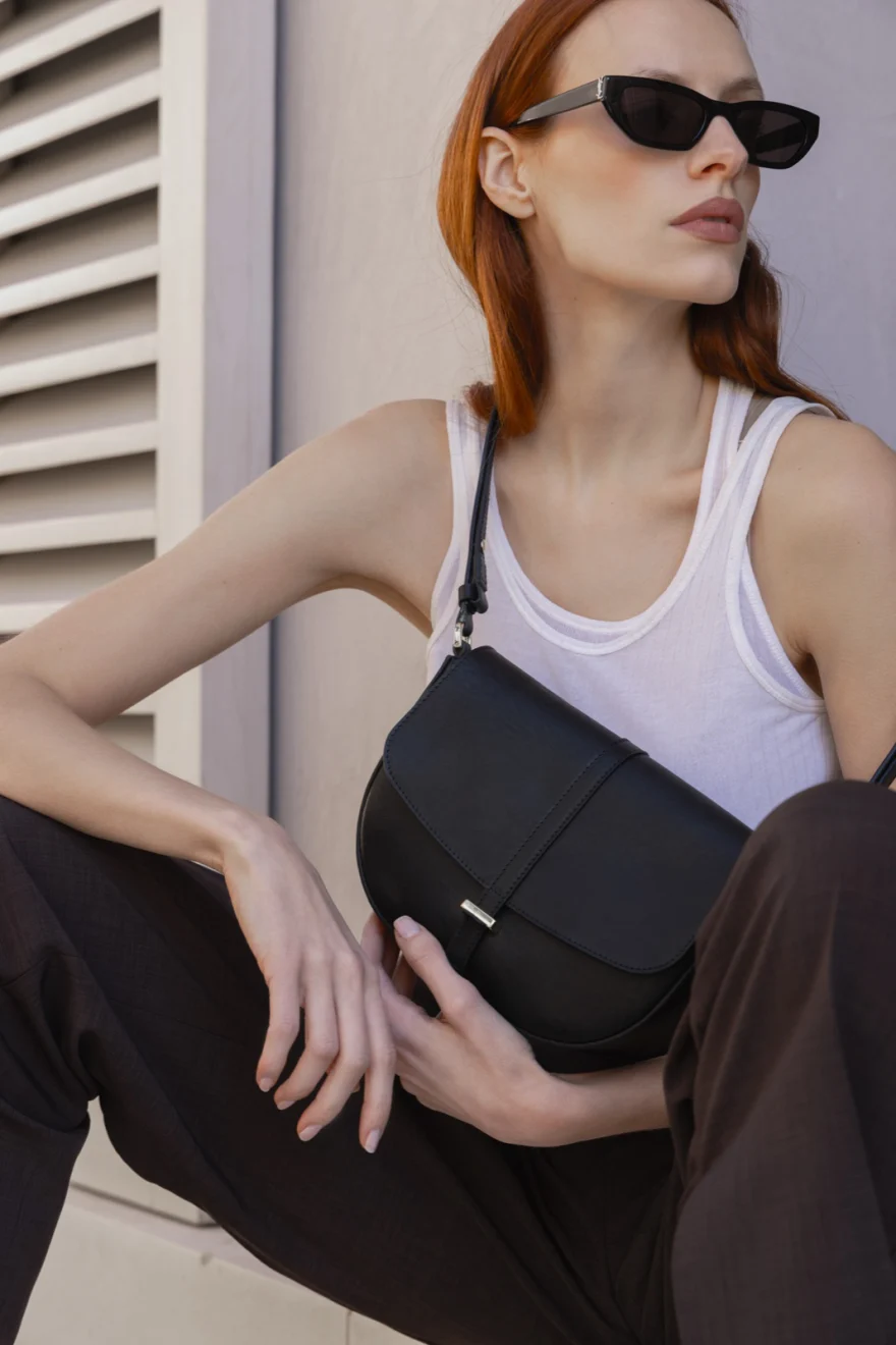 Model in sunglasses and a white top with a black shoulder bag, Biebi campaign photographed by Ina Cenusa