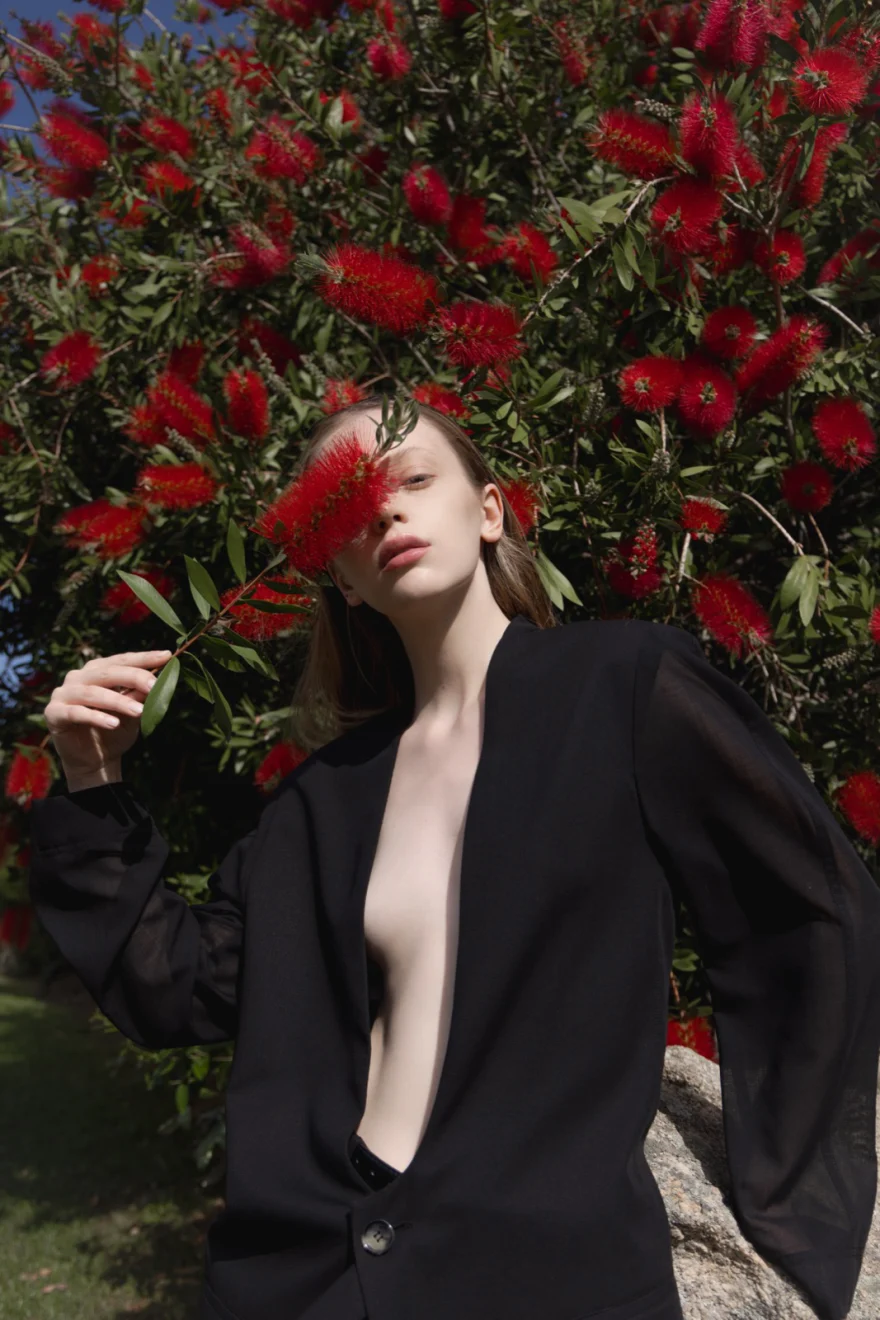 Model in a black jacket among red bottlebrush blossoms, SHOT Magazine editorial, photographed by Ina Cenusa