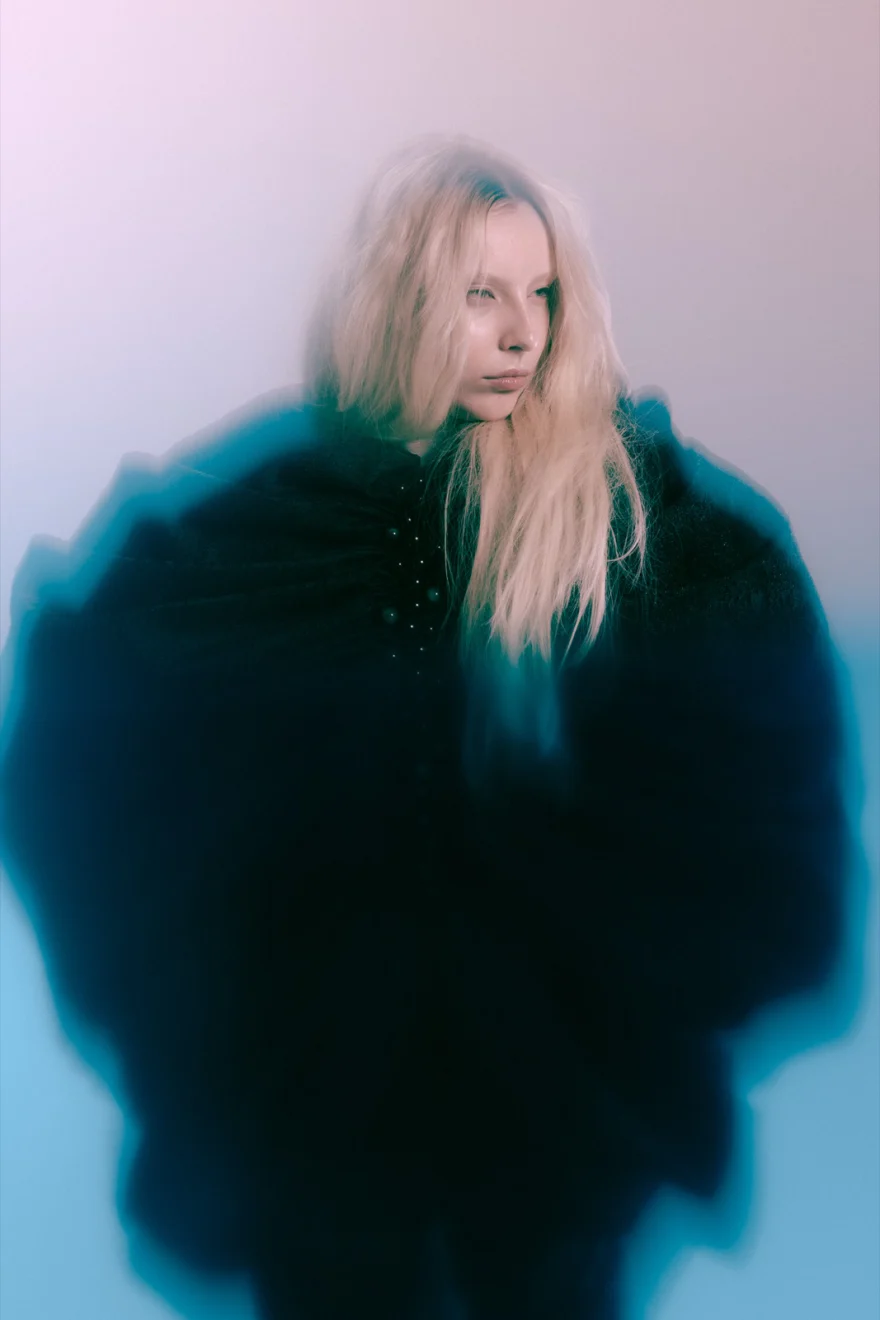 Model in a dark teal ruffled coat blurred by motion against a soft gradient, SHOT Magazine editorial photographed by Ina Cenusa