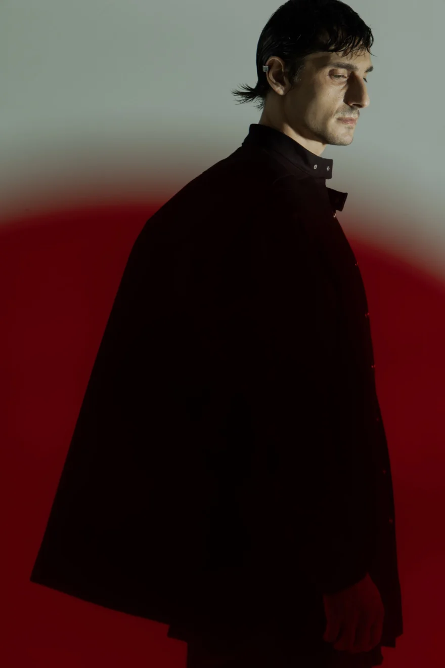 Male model in a red hooded cape on a red ground, Iso Model Management photographed by Ina Cenusa