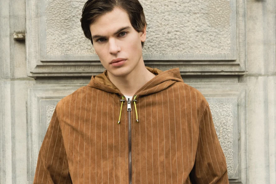Model in a tan corduroy hooded jacket against a stone facade, Pagani campaign in Geneva photographed by Ina Cenusa