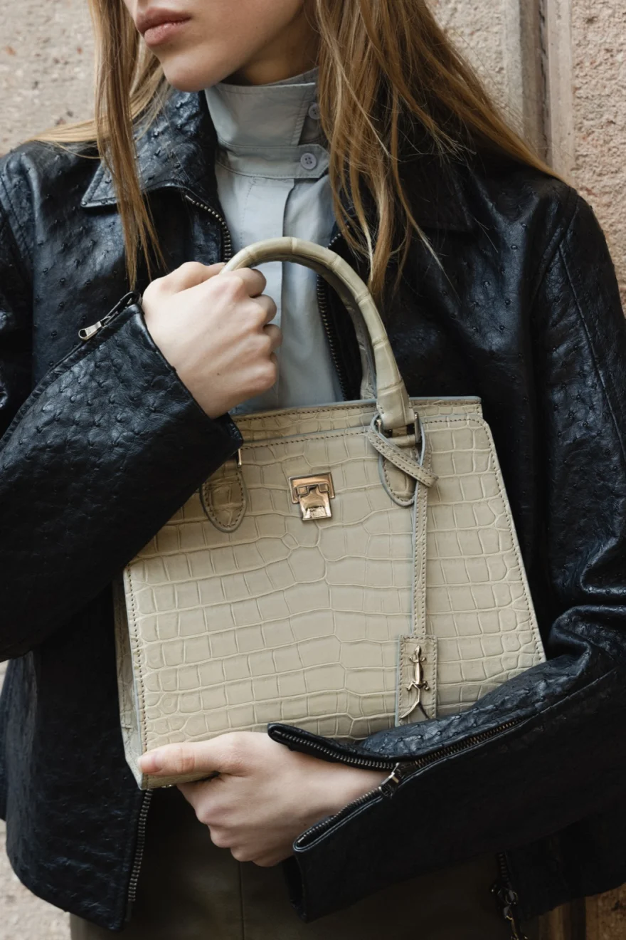 Detail of a grey crocodile-effect tote held against a black leather jacket, Pagani campaign in Geneva photographed by Ina Cenusa