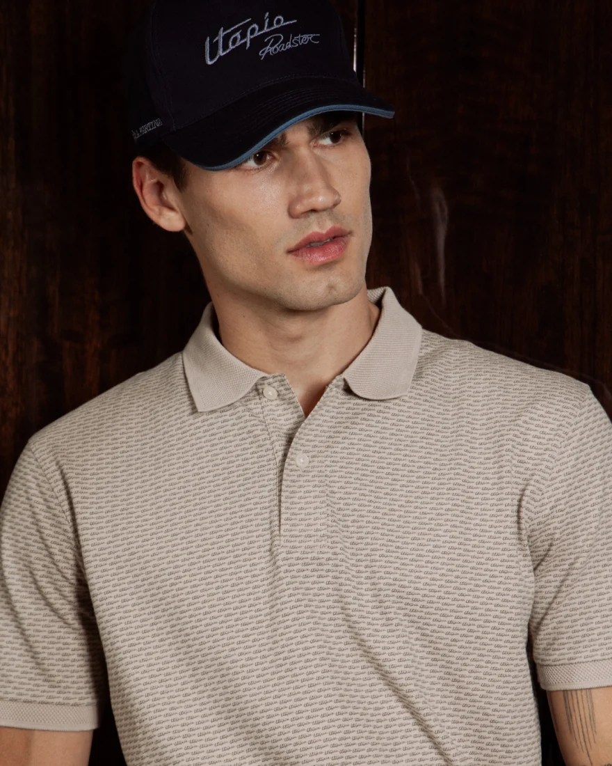 Male model in a navy cap and textured beige polo against dark wood, Pagani campaign in Geneva photographed by Ina Cenusa