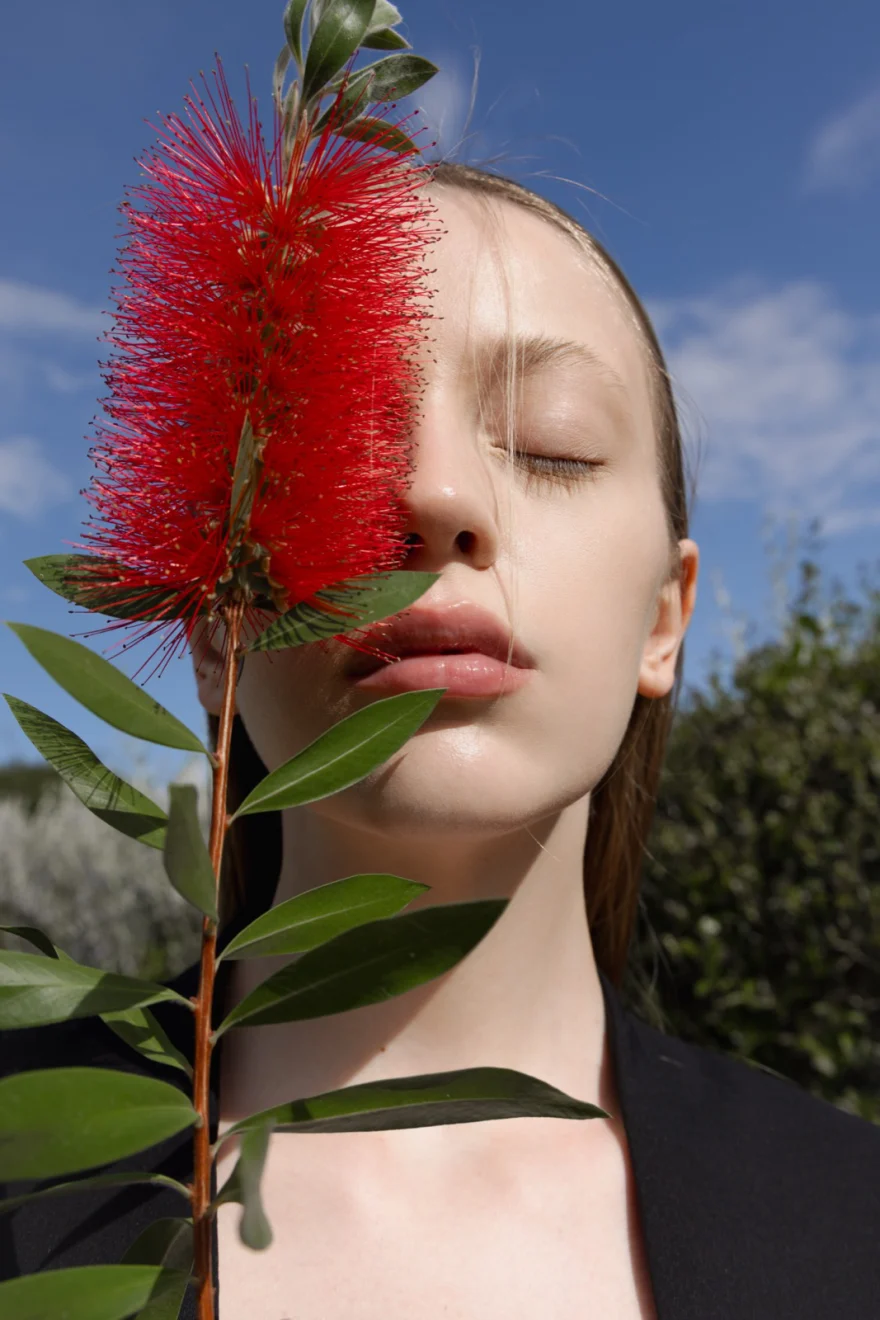 Model holding a red bottlebrush flower to her face against a blue sky, SHOT Magazine photographed by Ina Cenusa